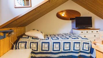 A bedroom with a sloped ceiling, a bed with a patterned bedspread, a television on a dresser, and a wall-mounted light fixture.