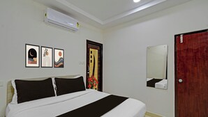 Habitación de hotel con una cama, aire acondicionado mural, una puerta con espejo y tres cuadros enmarcados.