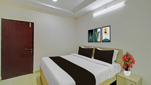 Una habitación de hotel con una cama, una mesita de noche, un florero y una puerta.