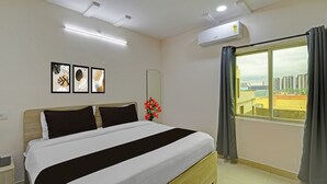 Una habitación de hotel con cama, ventana con cortinas, aire acondicionado y cuadros en la pared.