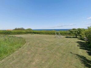 Eine grüne Freifläche mit einer Holz-Schaukel, einem Hecken und Blick aufs Meer.