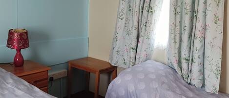 A bedroom with two beds, a desk, a lamp, and a wardrobe.