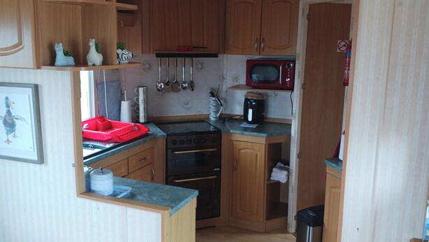 A compact kitchen with wooden cabinets, a stove, a microwave, and various kitchen utensils. - Donegal Mobile Home-coast-family Friendly-sleeps 5 (Gortahork)