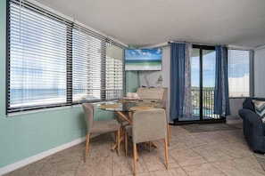 Une pièce comprenant une table à manger, des chaises, un téléviseur et donnant sur la mer.