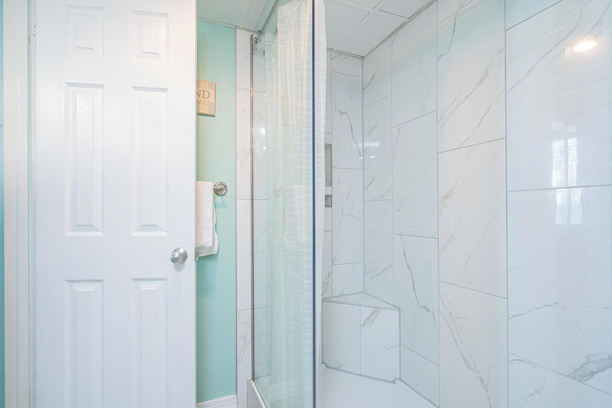 Une salle de bain avec une porte blanche, une cabine de douche en verre et des carreaux de marbre.