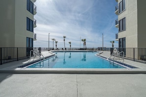 Une piscine à deux bassins, entourée d’une terrasse en béton et bordée d’une rambarde métallique.