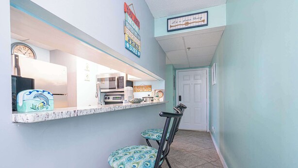 A kitchen with a refrigerator, microwave, and stove, a counter with a clock, and a door leading to another room. - Coastal Bliss Beachfront Resort Oasis for 5! (Panama City Beach)