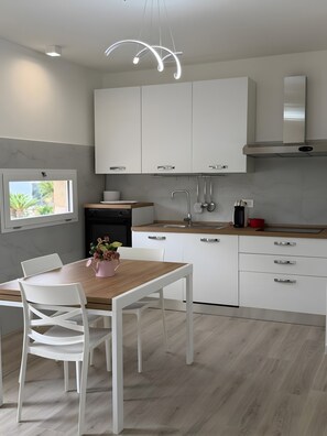 A modern kitchen with white cabinetry, a wooden dining table, and a pendant light. - Villa Matilde Domo Boutique - Barby Room (Torre degli Ulivi)