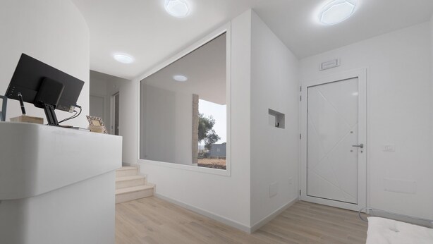 Quarto moderno com cama, escrivaninha com computador, porta e janela com vista.