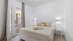 Quarto com cama, mesa de cabeceira e porta de correr para área externa.