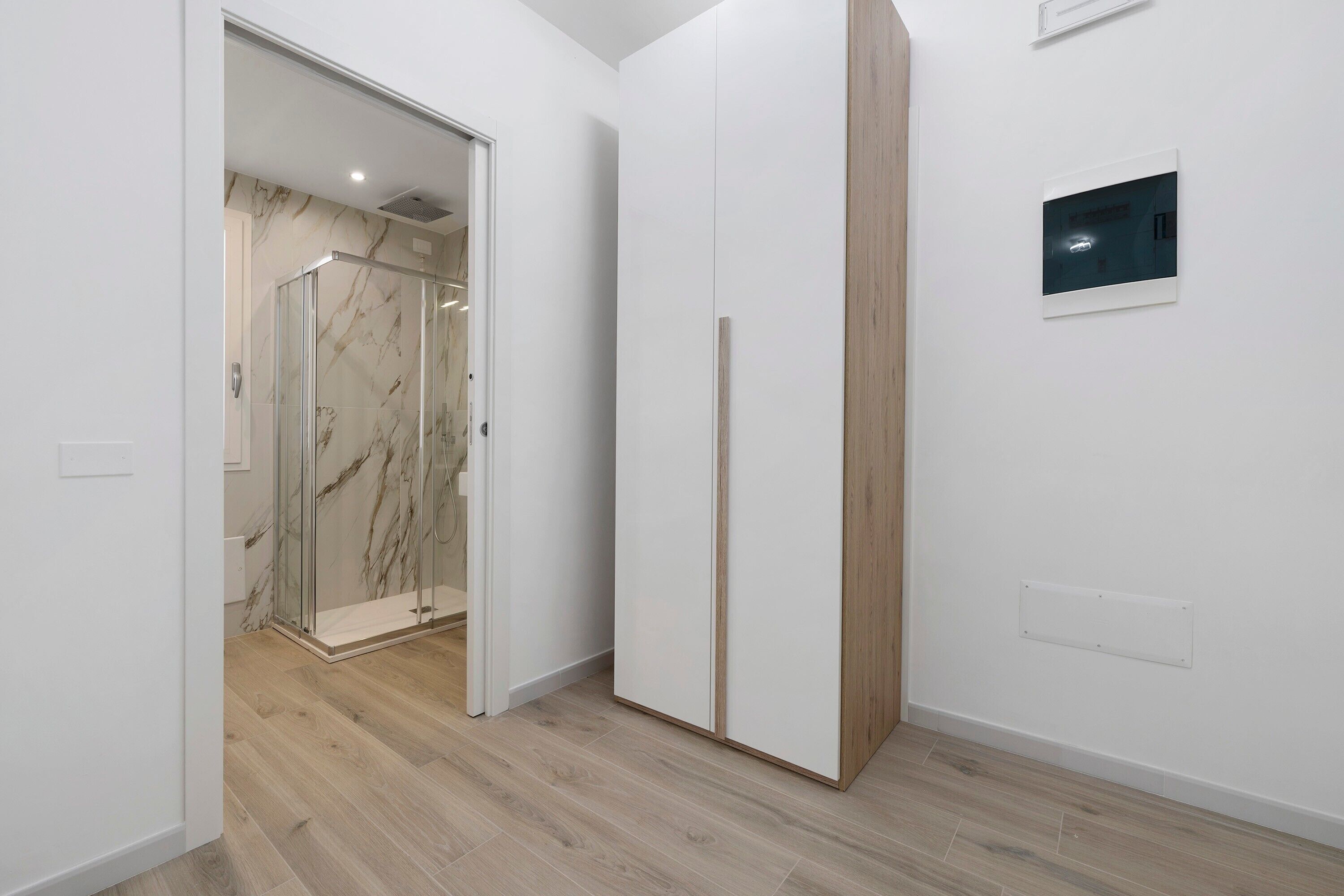Une chambre moderne avec une douche en verre, des murs blancs et un plancher en bois.