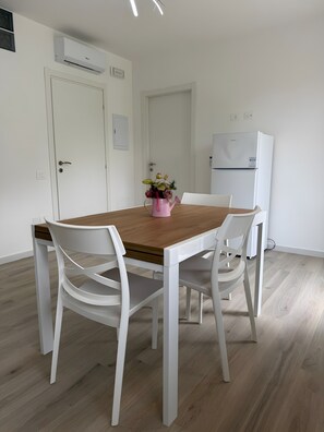 Ein Essbereich mit einem Holztisch, weißen Stühlen, einem Kühlschrank und einer Klimaanlage.