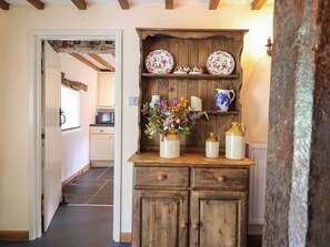 A rustic kitchen with wooden cabinets, a white countertop, and a shelf with decorative plates and a vase of flowers. - Frondirion (Machynlleth)