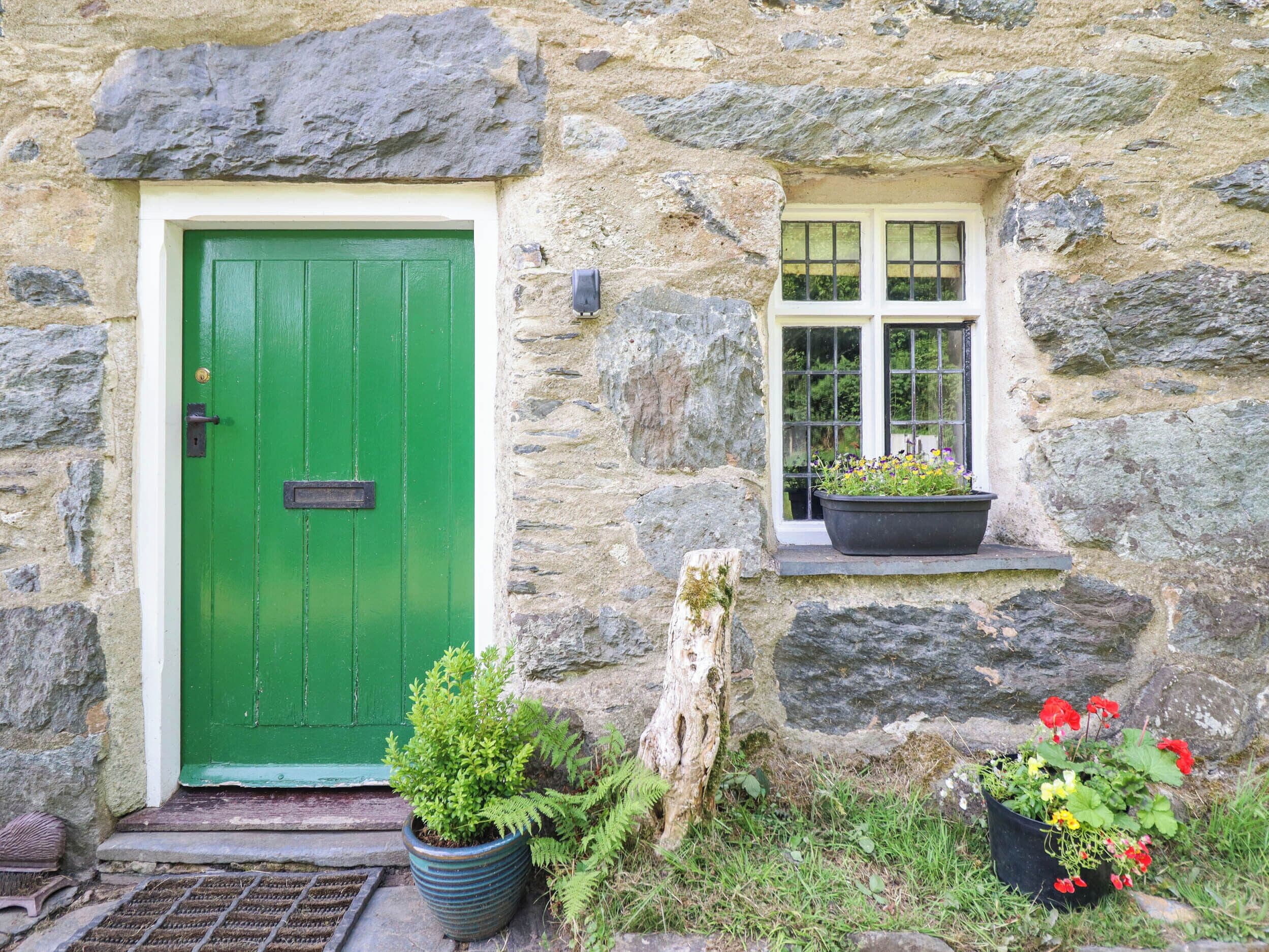 A stone building with a green door and a window with a potted plant.