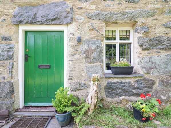 A stone building with a green door and a window with a potted plant. - Frondirion (Machynlleth)