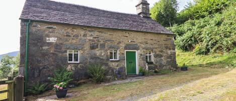 A stone cottage with a green door, a chimney, and a gravel path leading to the entrance.