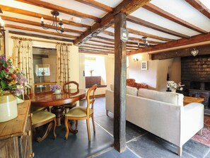 A rustic interior with exposed wooden beams, a dining area with a wooden table and chairs, a sofa, and a fireplace. - Frondirion (Machynlleth)
