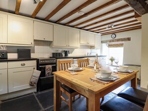 A kitchen with white cabinets, a wooden dining table set for two, and a black oven. - Frondirion (Machynlleth)
