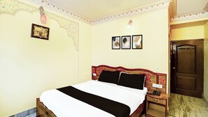 Une chambre à coucher comprenant un lit, des tables de chevet, une commode, une porte et un mur orné d’un motif floral et de trois tableaux encadrés.