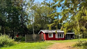 A red wooden cabin with a dirt path leading to it, surrounded by greenery and trees.