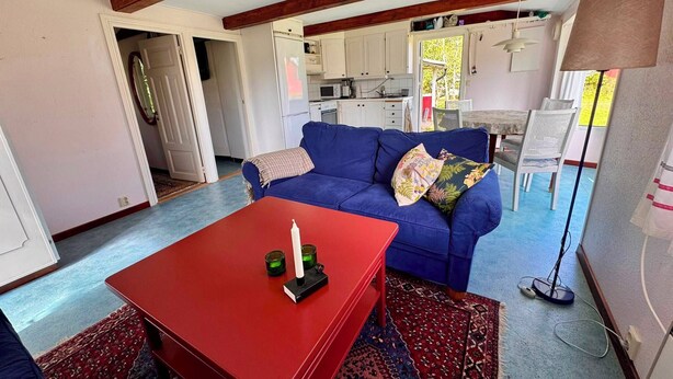 A living room with a red coffee table, blue sofa, and a kitchen in the background.