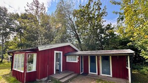 A red cabin with a porch and a small deck, surrounded by trees.