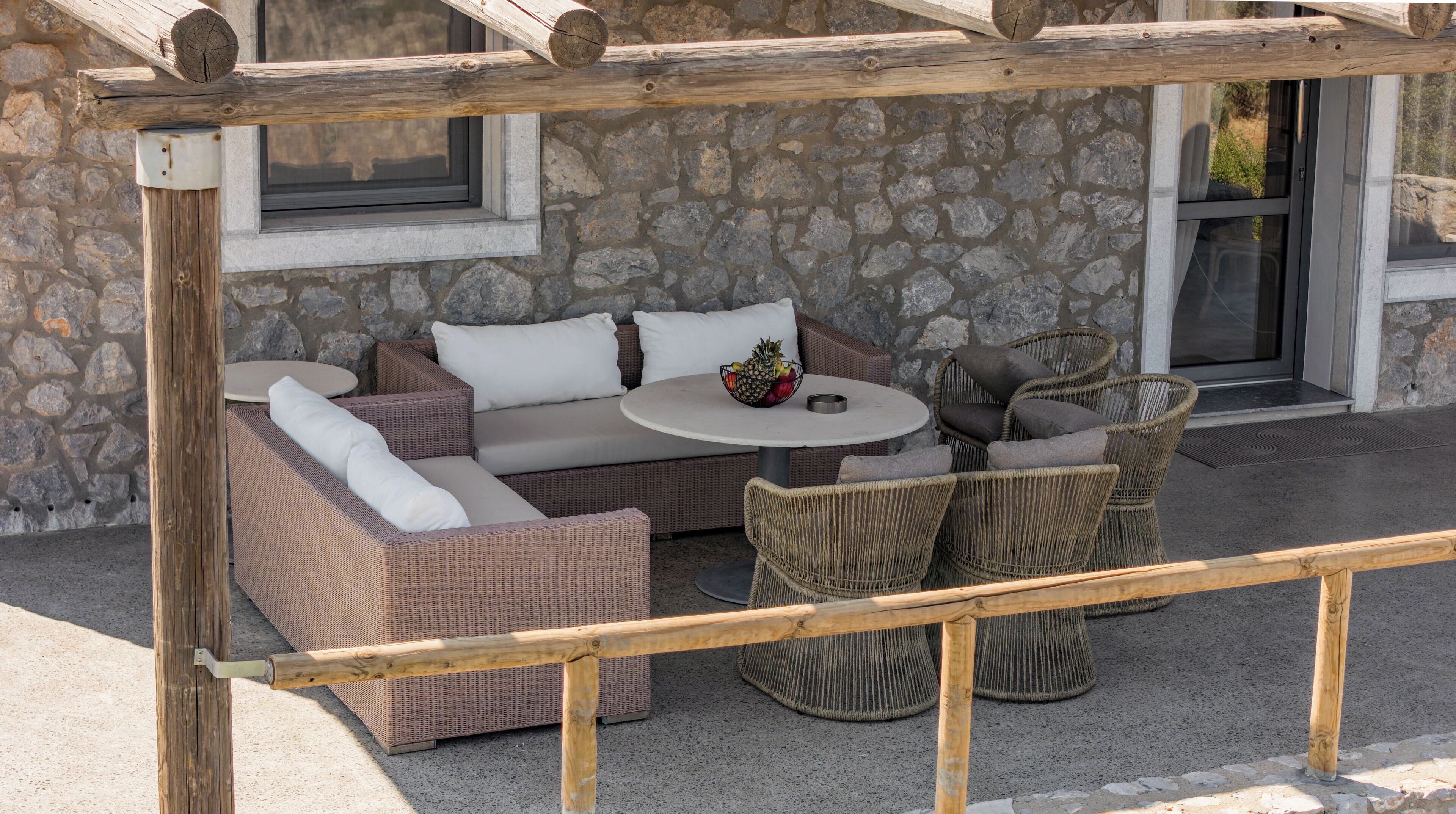 A covered outdoor seating area with wicker furniture, a stone wall, and a window.