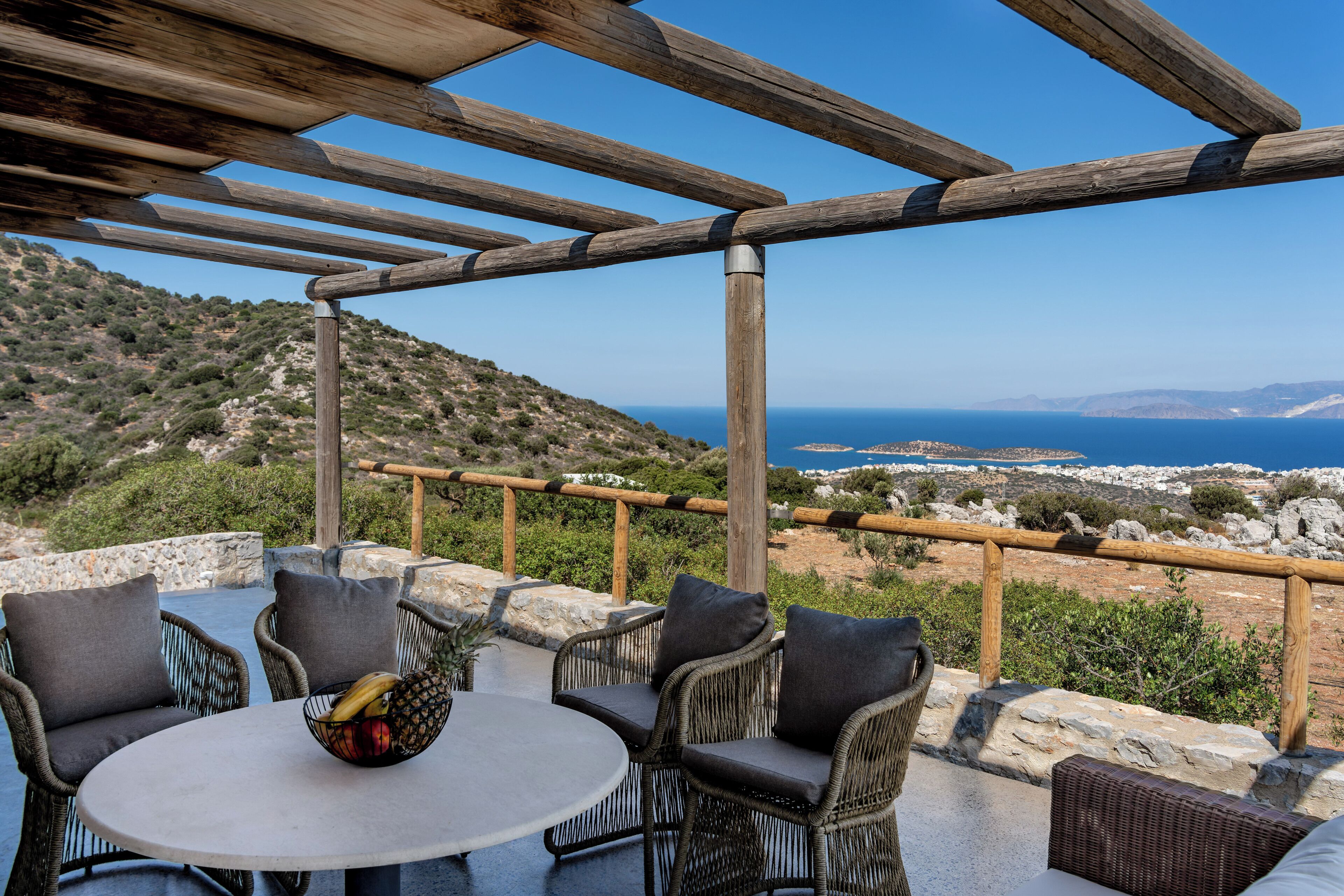 An outdoor seating area with wicker furniture and a table, overlooking a coastal landscape.