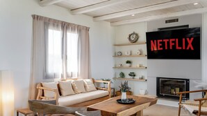 Ein modernes Wohnzimmer mit Sofa, Couchtisch, Sesseln, Kamin und einem an der Wand montierten Fernseher.