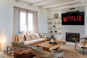 Ein modernes Wohnzimmer mit Sofa, Couchtisch, Sesseln, Kamin und einem an der Wand montierten Fernseher.