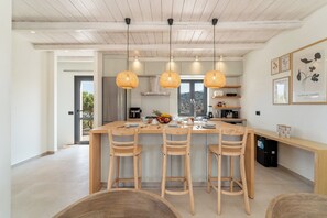 Een moderne keuken met een centraal eiland, houten stoelen, hanglampen en uitzicht door het raam.