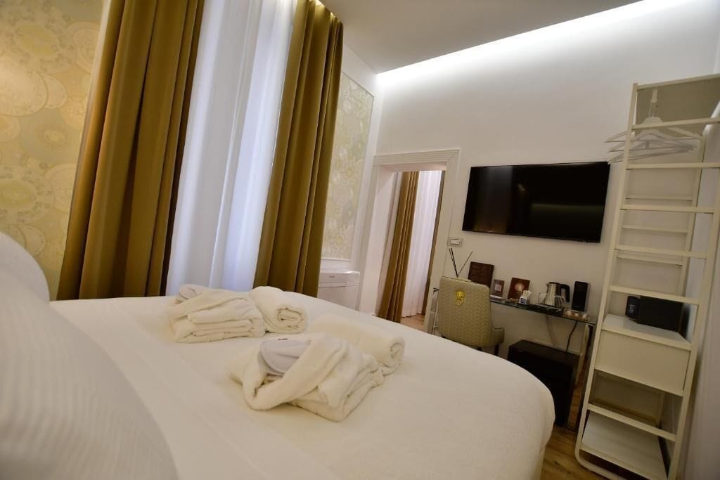 Quarto de hotel com cama, televisão na parede, escrivaninha com cadeira e guarda-roupa.