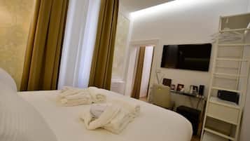 Quarto de hotel com cama, televisão na parede, escrivaninha com cadeira e guarda-roupa.