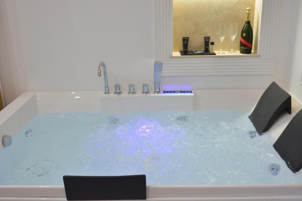 Une baignoire dotée d’un système de massage intégré, une fenêtre avec une bouteille de champagne et une étagère contenant des articles de toilette.