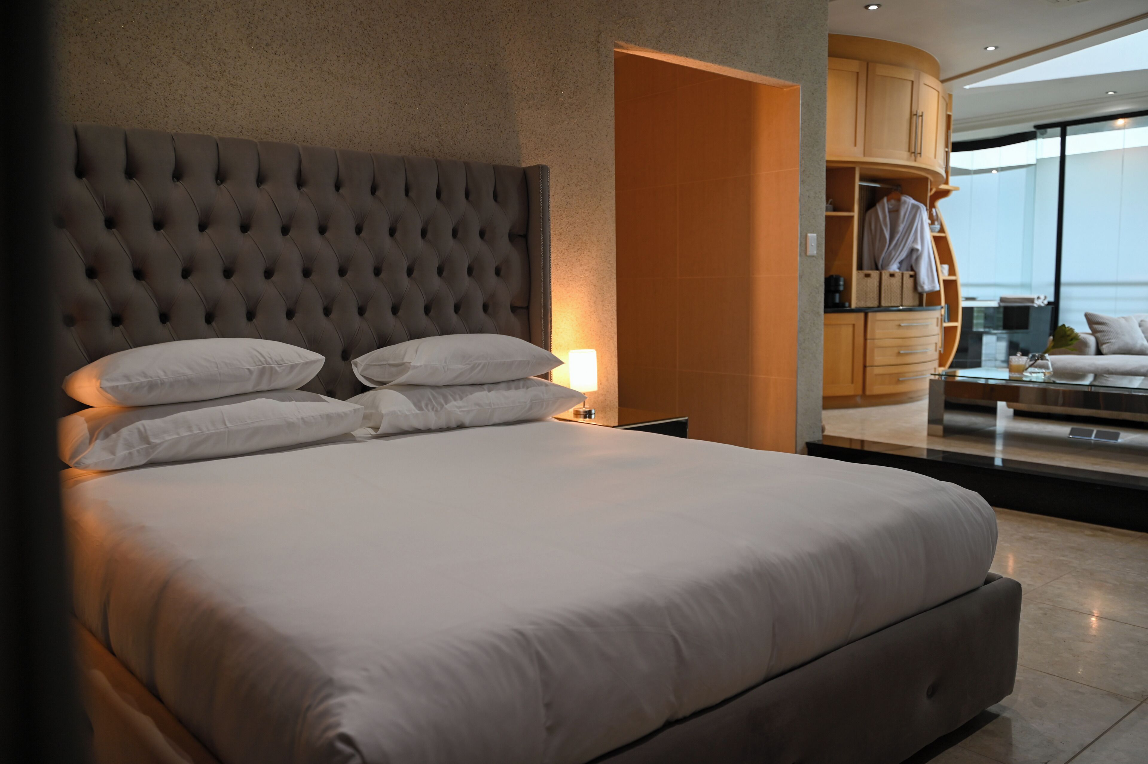 Quarto de hotel moderno com uma cama grande, cabeceira estofada e vista para a cidade através de uma janela ampla.