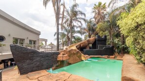 A pool area with a rock formation, palm trees, and a building in the background.