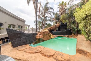 A pool area with a rock formation, palm trees, and a building in the background.