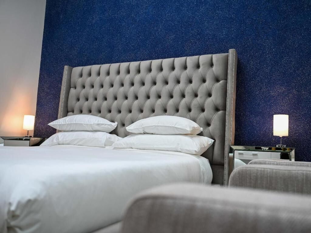 Habitación de hotel con tablero de cabecera acolchado, ropa de cama blanca y dos lámparas de noche.