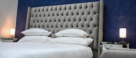 Habitación de hotel con tablero de cabecera acolchado, ropa de cama blanca y dos lámparas de noche.