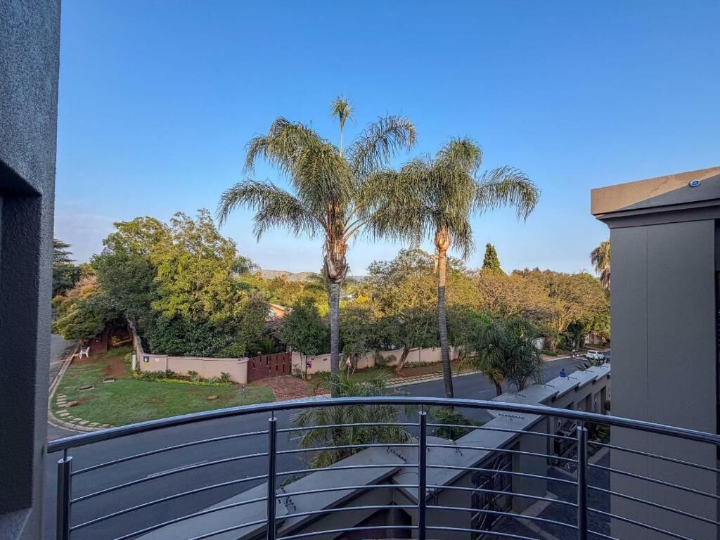 A balcony with a metal railing overlooking a garden with palm trees and a clear sky.