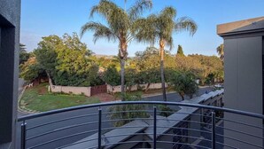 A balcony with a metal railing overlooking a garden with palm trees and a clear sky.