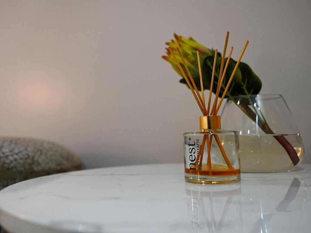 A clear glass bottle with a label, a flower, and a glass on a reflective surface.
