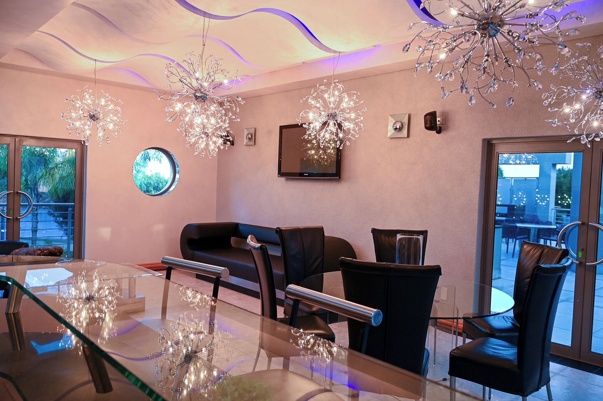 A modern dining area with a glass table, black chairs, and decorative crystal chandeliers.
