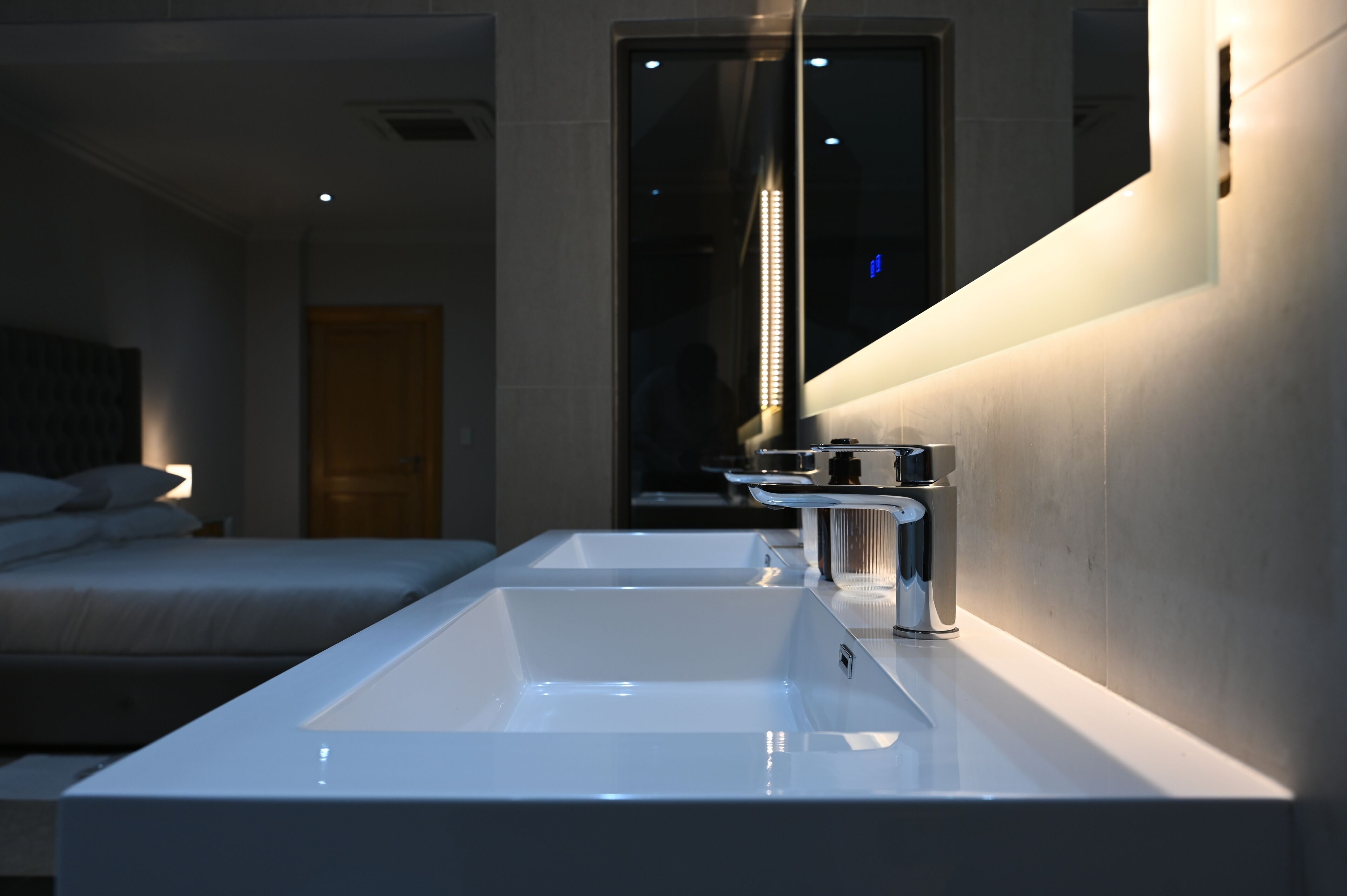 A modern bathroom with a large sink, a mirror, and a bed in the background.