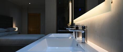 A modern bathroom with a large sink, a mirror, and a bed in the background.