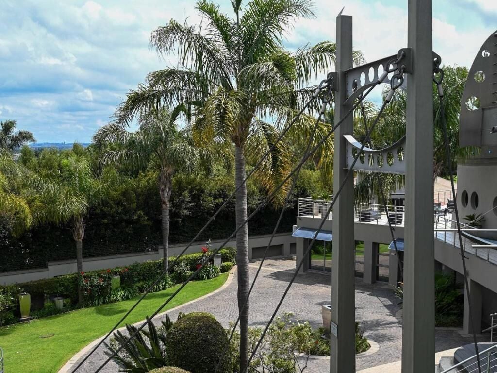 Un edificio moderno con balcón que da a un jardín ajardinado con palmeras.
