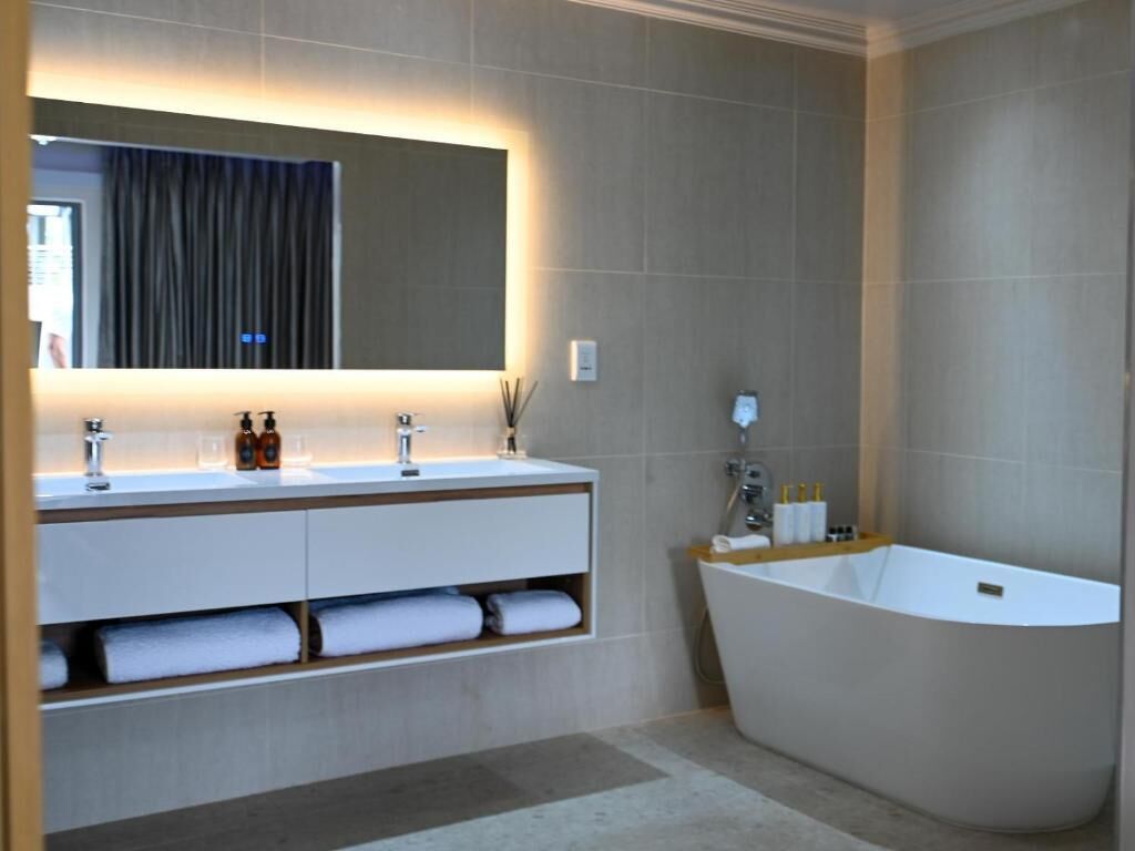 A modern bathroom with a freestanding bathtub, a large mirror, and a vanity with multiple sinks and storage.