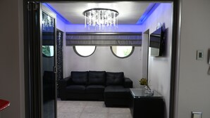 A modern living room with a black leather sofa, a glass coffee table, and a chandelier.