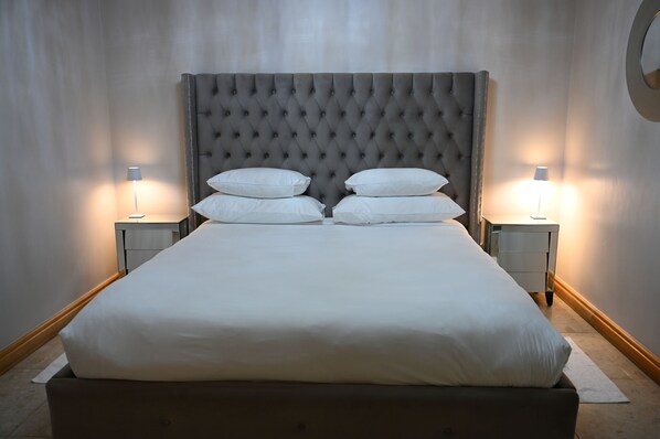 A bed with a tufted headboard, two bedside tables with lamps, and a plain wall.