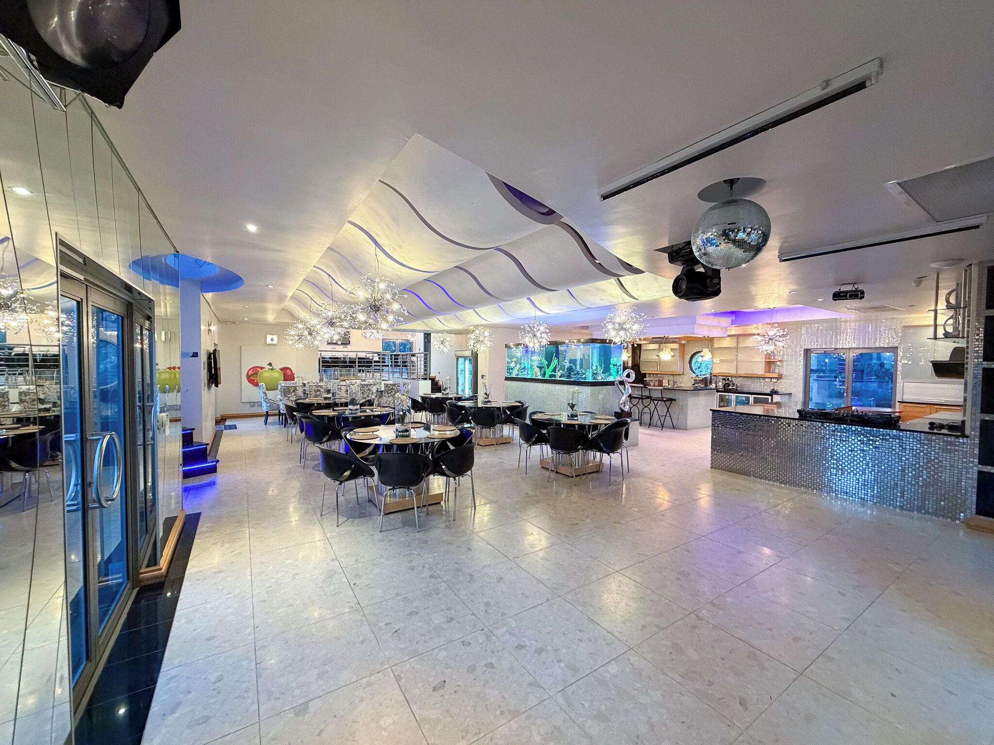 Un restaurante amplio con varias mesas y sillas, una zona de bar y una gran acuario.